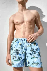 Short de baño celeste con estampado de palmeras, personas y paisajes playeros. Tiene elástico en la cintura y cordón de ajuste.