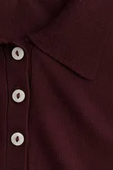 Sweater de punto fino color bordó, con cuello polo y tapeta de botones. Presenta hombros ligeramente caídos y remates acanalados en puños y bajo.