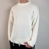 Sweater tejido color crudo, de corte holgado, con cuello redondo y terminaciones rotas en puños y ruedo.