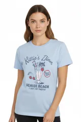 Remera celeste de algodón con cuello redondo y mangas cortas. Estampado frontal con la leyenda "Kittie's Diner Venice Beach" y dibujo de un gato en un milkshake.