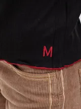 Polera negra de tela rib con cuello alto y mangas largas. Presenta pespuntes rojos en cuello, hombros y puños.
