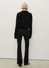 Pantalón de jean negro de tiro medio, corte ajustado hasta la rodilla y acampanado en la parte inferior, con bajo deshilachado.