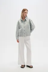 Campera de jean color crudo, de corte recto, con cuello clásico, cierre frontal con botones metálicos, dos bolsillos con solapa en el pecho y bajo con detalle de bordado calado.