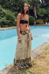 Falda larga color crema con estampado floral en tonos negro y dorado, cintura elástica con cordón ajustable y borlas decorativas.