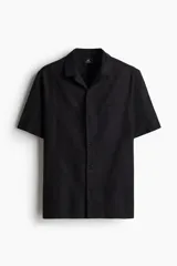 Camisa negra de manga corta en mezcla de algodón y lino. Modelo con cuello abierto, tapeta lisa y bolsillo superior abierto.