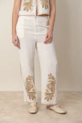 Pantalón de lino color crudo con bordado floral color camel en el ruedo y costados. Tiene bolsillos laterales y cintura elástica.