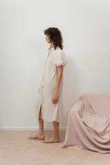 Vestido color beige con botones frontales, cuello camisero, mangas cortas abullonadas y falda con volantes.