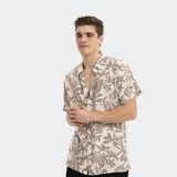Camisa de manga corta con estampado tropical en tonos beige y blanco, con cuello clásico y cierre frontal con botones.