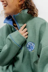 Buzo verde y azul con cierre metálico y bordados de flores.