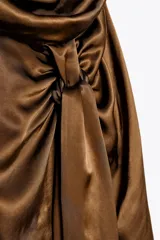 Vestido midi color marrón de satén, con cuello halter fluido y espalda descubierta. Presenta un nudo en la parte delantera, abertura frontal y cierre trasero con cremallera oculta.
