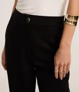 Pantalón zanahoria de poliéster color marrón, de cintura alta, con cierre tradicional, bolsillos traseros y botón metalizado con efecto martillado.