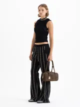 Cartera rectangular de estructura firme confeccionada en cuero descarne vacuno color marrón. Presenta manijas fijas, cierre superior y un charm metálico dorado en forma de vaquita de San Antonio colgando de un tag lateral. Incluye el logo de la marca grabado en relieve en el frente.