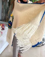 Ruana de lana merino color crudo, tejida y bordada a mano con el escudo de Uruguay en la espalda. Tiene calce holgado y flecos en el ruedo.