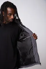 Campera puffer gris con la parte superior negra, cierre frontal y cuello alto.