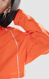 Remera corta naranja con mangas cortas abullonadas y ribete blanco en cuello, mangas y laterales.