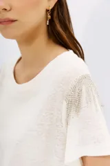 Remera blanca de lino con mangas cortas y calce al cuerpo. Presenta cadenas de strass en los hombros.