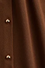 Chaleco corto marrón de punto, con cuello redondo y botones dorados en el frente.