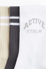 Pack de cinco pares de medias deportivas de caña media en punto fino suave de tejido funcional confeccionado con DryMove™, que ayuda a absorber el sudor y mantenerse frescos. Incluye un par negro, un par beige con una raya blanca, un par blanco con una raya gris, un par gris con dos rayas blancas y un par marrón con la inscripción "ACTIVE STHLM" en blanco.