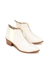 Botines color crema con textura tipo piel de cocodrilo, cierre frontal con cremallera dorada, paneles laterales elásticos y tacón de bloque en madera clara.
