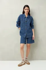 Sobrecamisa oversize de jean azul con cuello camisero, cierre frontal con botones, mangas largas y bolsillos de parche en el pecho.