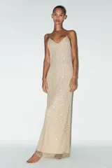 Vestido largo color dorado, confeccionado en tejido tipo red con aplicación de strass, escote pico y tirantes finos. Incluye forro interior y cierre en espalda con cremallera oculta en costura.