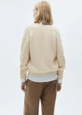 Sweater color crema de tejido de punto grueso con diseño trenzado, cuello en V y corte recto.
