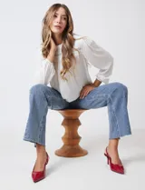 Blusa blanca de gasa plisada con encaje calado en el cuello y el pecho. Cuello a la base fruncido, manga larga con puño elastizado y espalda lisa con abertura tipo gota y botón.