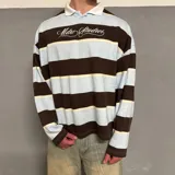 Buzo tipo polo de manga larga a rayas horizontales en color celeste, marrón y crema, con cuello blanco y logo bordado en el pecho. Corte boxy.