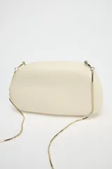 Bolso formato caja color crema con asa de cadena dorada para usar como bandolera. Cierre metálico dorado.