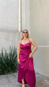 Vestido midi fucsia de satén con escote drapeado, breteles finos y falda cruzada con volados.