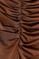 Vestido midi marrón de poliéster, con escote asimétrico y un solo hombro descubierto. Presenta detalle de frunces en la parte delantera y abertura lateral en el bajo.