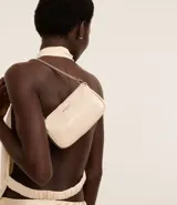 Cartera baguette pequeña color crema, confeccionada en PU glossy con asa corta de cadena plateada desmontable. Forro de poliéster.