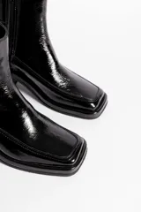 Bota corta de cuero charol negro, con caña baja, cierre lateral y taco cuadrado de madera.