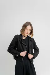 Chaqueta negra tipo biker de gamuza sintética con cuello solapa y manga larga con trabillas en los hombros. Tiene bolsillos delanteros con cremallera metálica y cierre frontal con cremallera.