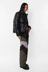 Campera puffer negra de cuerina PU opaca, corte boxy fit, cuello alto con elástico y tancas metálicas, acceso delantero con cierre metálico desmontable y tiracierre de marca, bolsillos ribete con snap metálico y bolsillo superior con cierre metálico cubierto por vista y avío marcario, mangas desmontables por cierre de nylon cubierto con vista, terminaciones de mangas y cintura con elástico interno, forrería al tono, cinta gross estampada nombre de marca y snaps en sus extremos para transportarla al hombro, bolsillo interno de tela base con cierre invisible.
