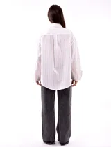 Camisa blanca con rayas verticales negras, de corte holgado, manga larga con puños abotonados y bolsillo en el pecho.