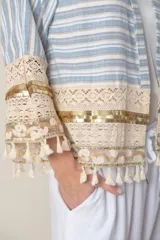 Chaqueta corta de jean rayada en tonos celeste y blanco, con apliques de puntilla y flecos en ruedo y mangas.