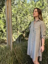 Vestido camisero color gris topo, de lino 100% natural, con botones de nácar, bolsillo delantero y mangas largas con botón para recogerlas. Diseño asimétrico más largo en la parte trasera.