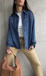 Sobrecamisa de denim azul con bordados florales en cuello y hombros, cierre frontal con botones azules y corte holgado.