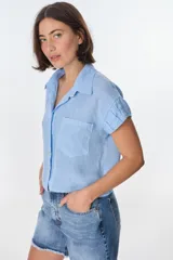 Camisa color beige de lino, con cuello clásico, manga corta con detalle de frunce y bolsillo de parche en el pecho.