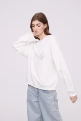 Buzo blanco de corte holgado con cuello redondo y mangas largas. Presenta un pequeño estampado de una flor en el centro del pecho.