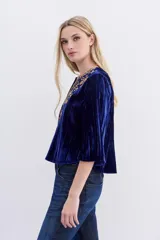 Camisa azul de velvet con bordados dorados de lurex en el pecho y la espalda, detalles de mostacillas y lentejuelas doradas, mangas largas y escote redondo con abertura frontal.
