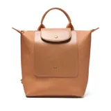 Mochila color habano de material símil cuero (PU) con interior textil rosa viejo. Presenta un asa corta superior, correas traseras regulables y herrajes metálicos dorados. Posee un bolsillo interno con cierre y un bolsillo frontal con solapa y broche metálico.