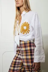 Camisa blanca de lino con bordado de sol amarillo con corazón en el bolsillo.