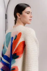 Ruana de tejido de punto color crema, con diseño abstracto bordado en la espalda en tonos celeste, rosa, naranja, azul y violeta.