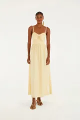 Vestido largo color amarillo pálido, de tirantes finos con detalle de volados, escote recto y lazo decorativo en el busto.
