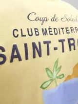 Musculosa sin mangas, color crema, con cuello redondo y calce relajado. Presenta un estampado gráfico en la espalda con texto en francés que hace referencia a Saint-Tropez y una ilustración de una bebida tropical.