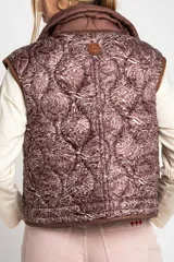 Chaleco marrón acolchado con cuello alto, cierre frontal con broches a presión y dos bolsillos delanteros con cordón ajustable.