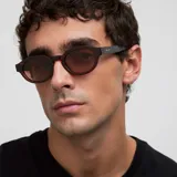 Lentes de sol con montura geométrica en color bordó translúcido y cristales ovalados marrones. Presentan un diseño de inspiración retro con la parte superior plana y la parte inferior redondeada, fabricados con materiales bio-basados y lentes polarizadas TAC con protección UV400.