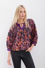 Camisa de corte amplio con estampado animal print en tonos naranja, marrón y violeta, con escote en V con lazos para atar y mangas 3/4 abullonadas.